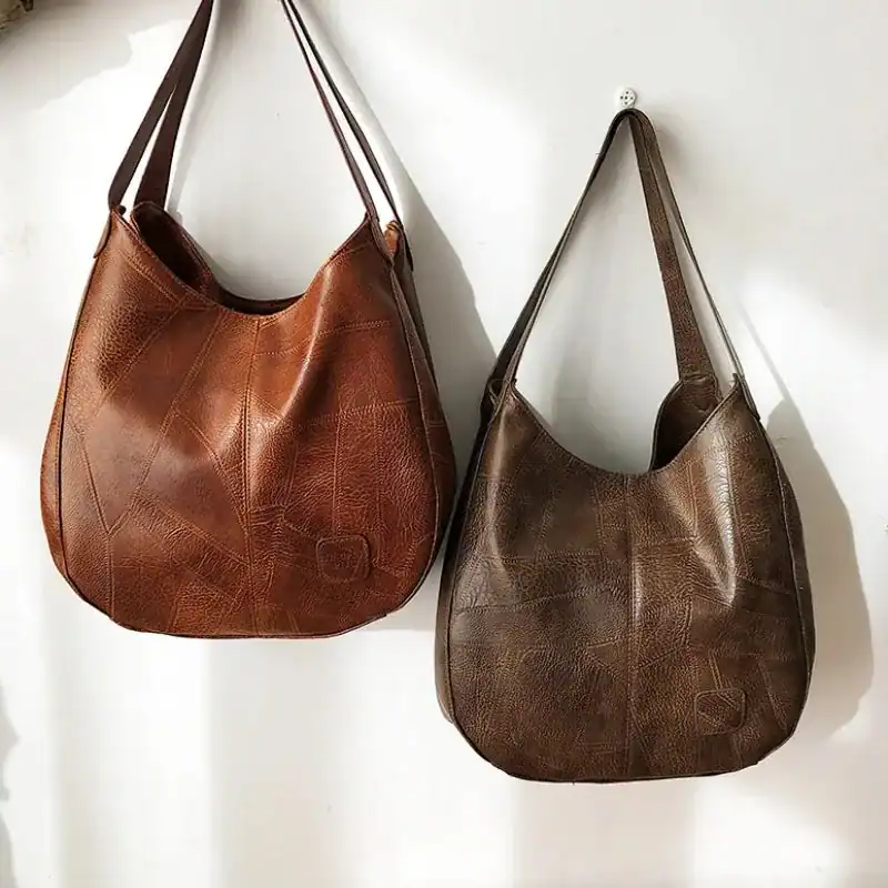 Metallic hobo väska i brunt och mörkbrunt, läderliknande material, hängande på vägg.