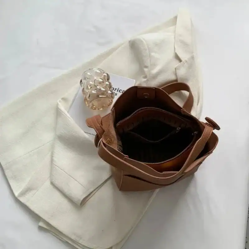 Mörkbrun hinkväska med öppen topp och inre ficka, placerad på vit tygduk.