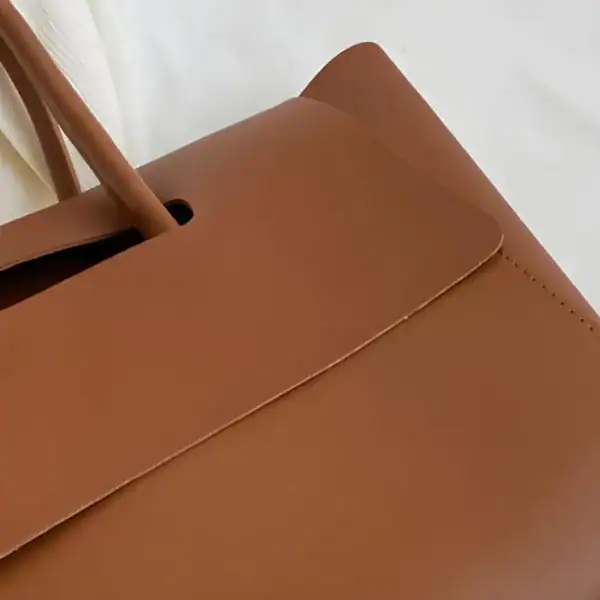 Mörkbrun shopper axelväska med läderhandtag och exakt sömnad.