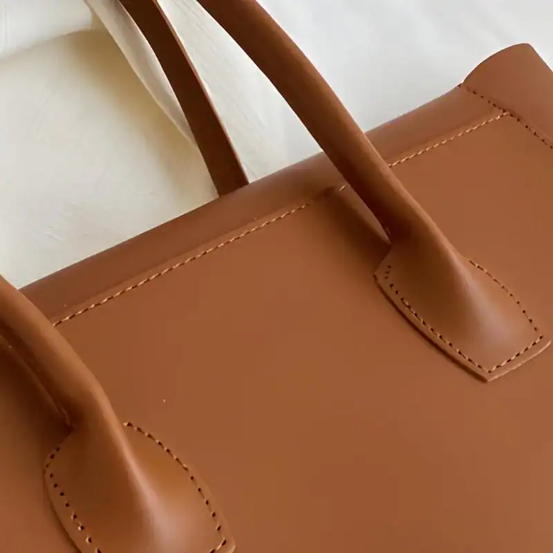 Mörkbrun shopper med tydlig näsning och handtag, läderhandväska.