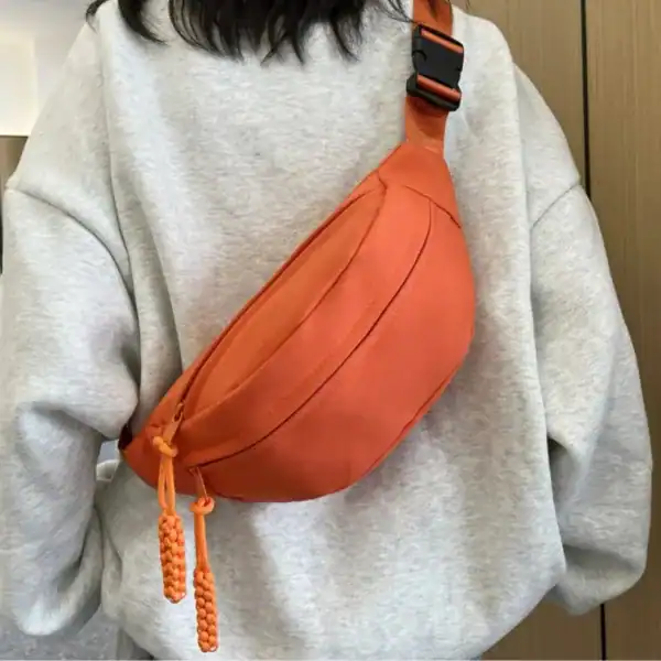 Orange nylon midjeväska med svart rem, bärt av person i grå tröja.