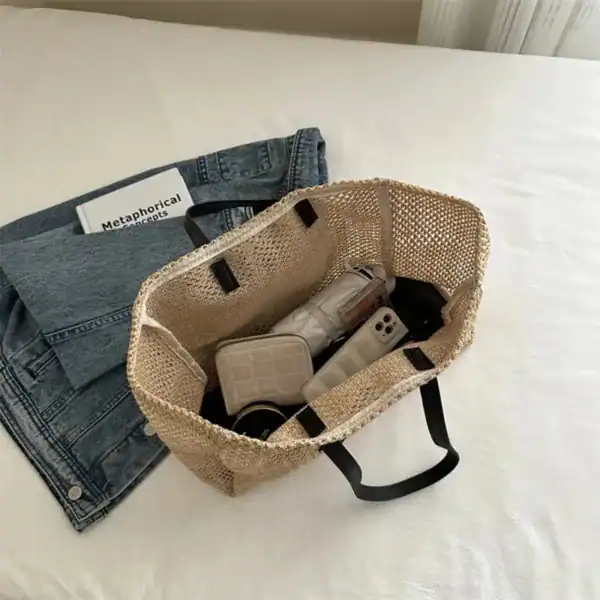 Raffia shoppingväska med svarta handtag och innehåll på vit säng.
