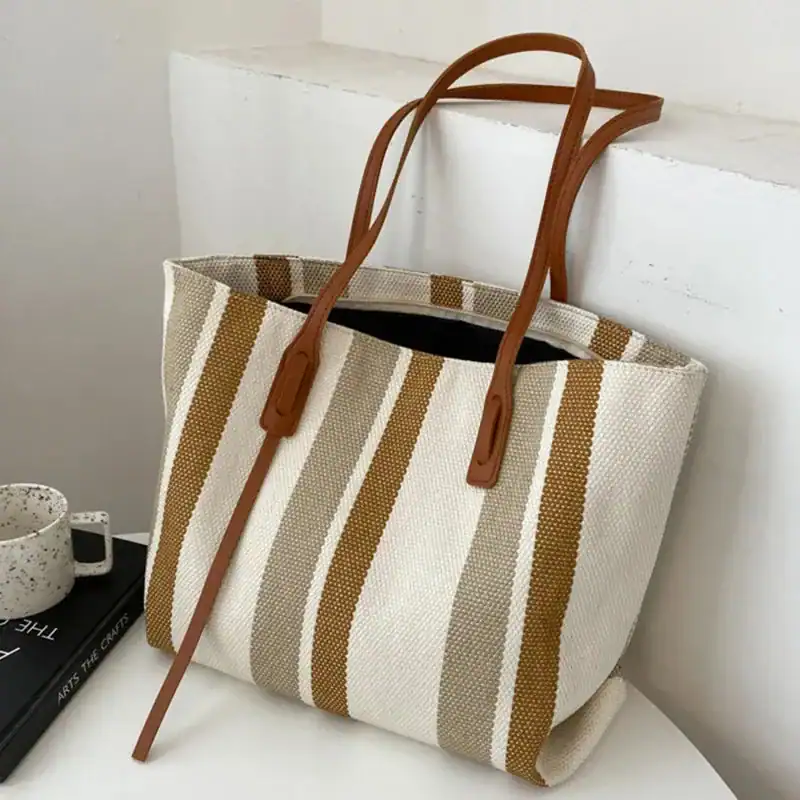 Randig svartvit shoppingväska med bruna handtag och stilren design.