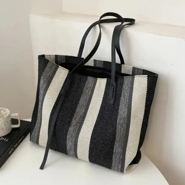 Randig svartvit shoppingväska med svarta handtag och stilrent mönster.