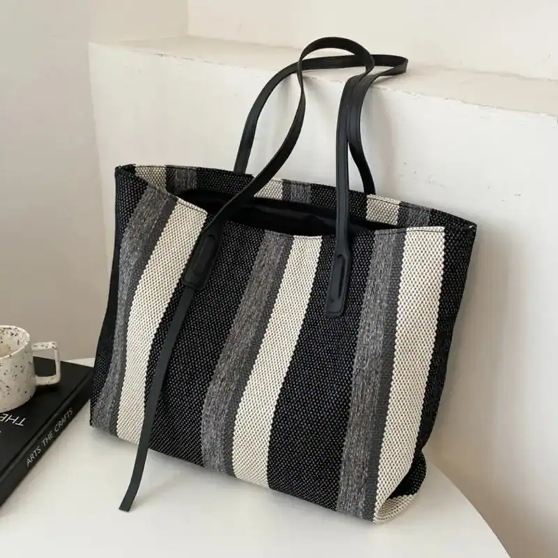 Randig svartvit shoppingväska med svarta handtag och stilrent mönster.