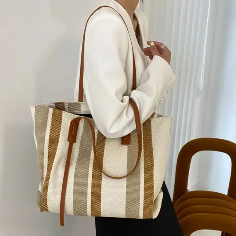 Randig svartvit shoppingväska med bruna handtag och stilren design.