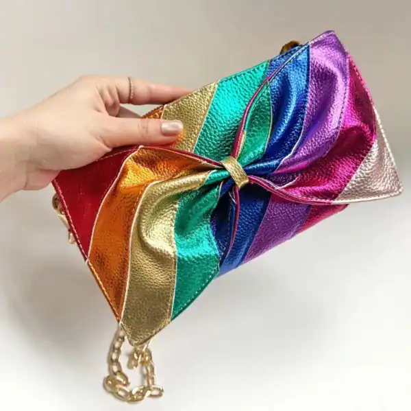 Regnbågsfärgad clutch med stor rosett och kedjehandtag.