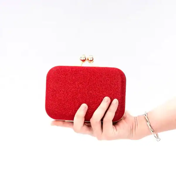 Röd glitterclutch med guldlock, hållen i handen.