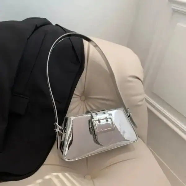 Silver metallic axelremsväska med buckel och svart jacka på beige soffa.