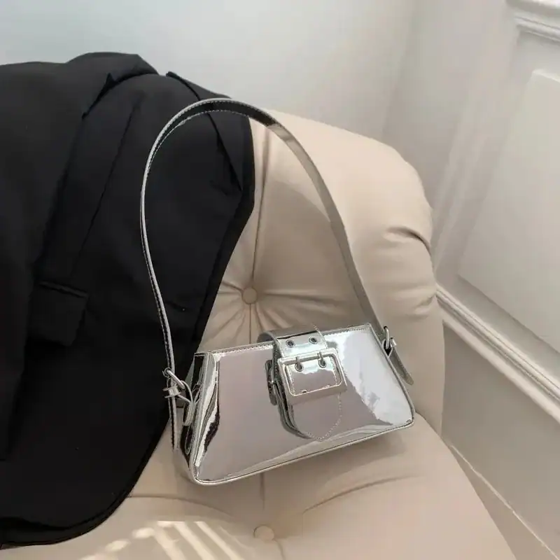 Silver metallic axelremsväska med buckel och svart jacka på beige soffa.