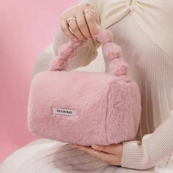 Rosa fluffig väska med pärlformade handtag och etikett.