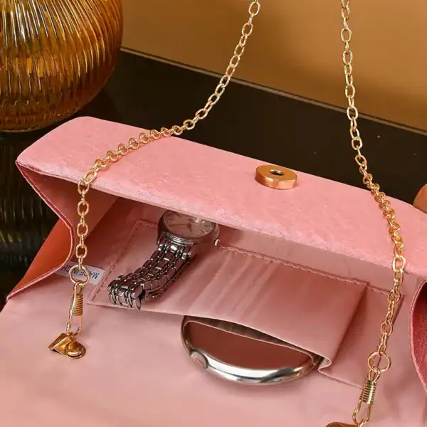 Rosa kuvertväska med gyllene kedja och innehåll som klocka och handväska.