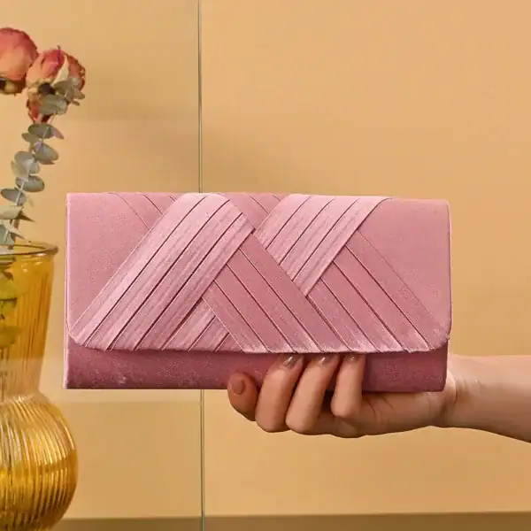Rosa kuvertväska med vävad textur, hållen i handen mot varm bakgrund.