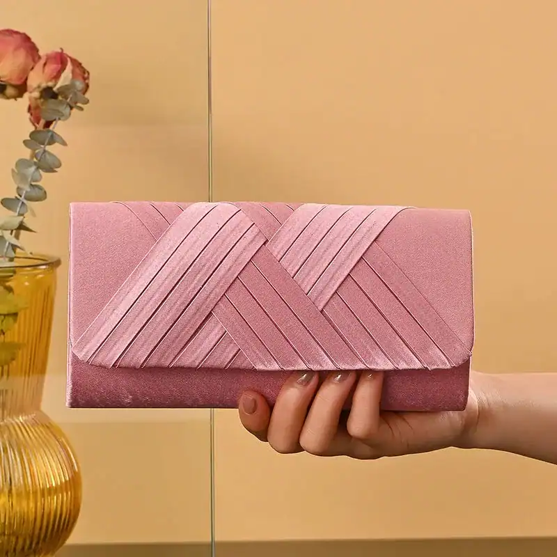 Rosa kuvertväska med vävad textur, hållen i handen mot varm bakgrund.