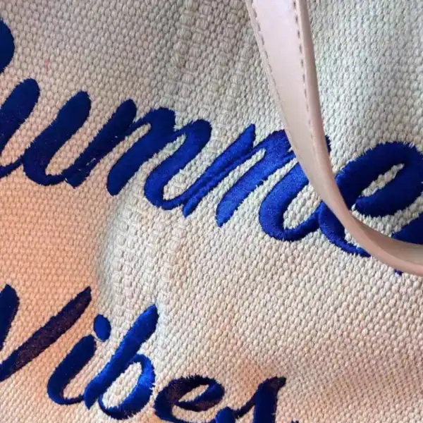 Rosa strandväska med blå text Summer Vibes, närbild på tyg och handtag.