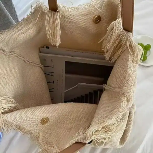 Strandväska i beige med fransar och text, perfekt för sommar och strand.