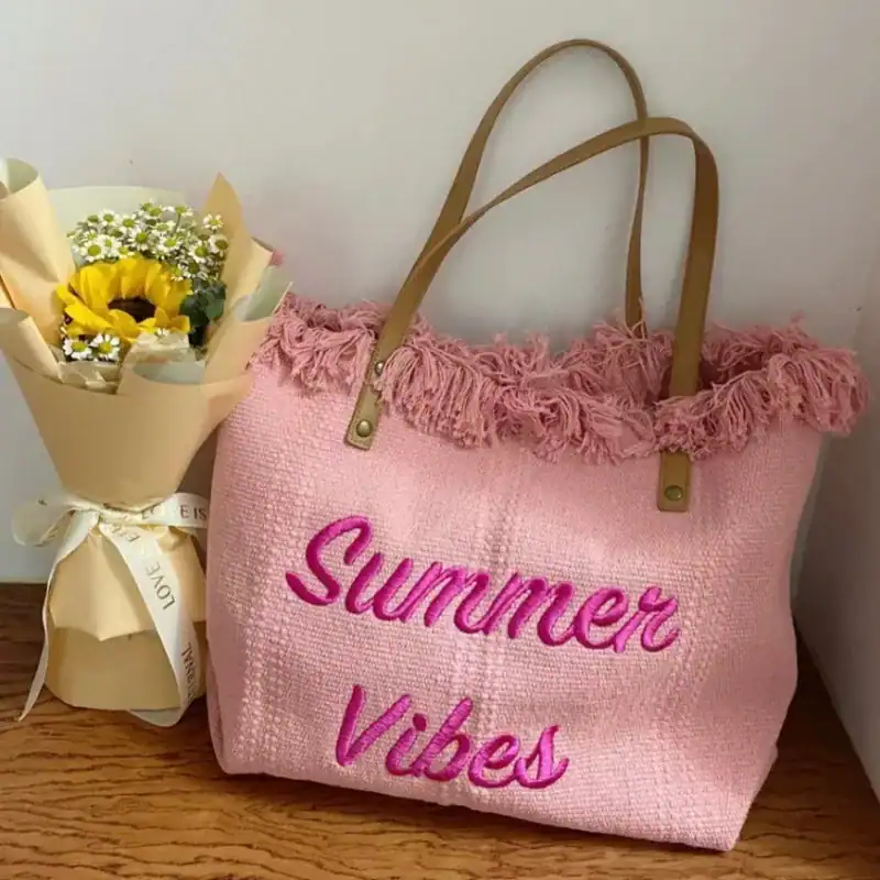 Rosa strandväska med text Summer Vibes och fransar, perfekt för sommar.
