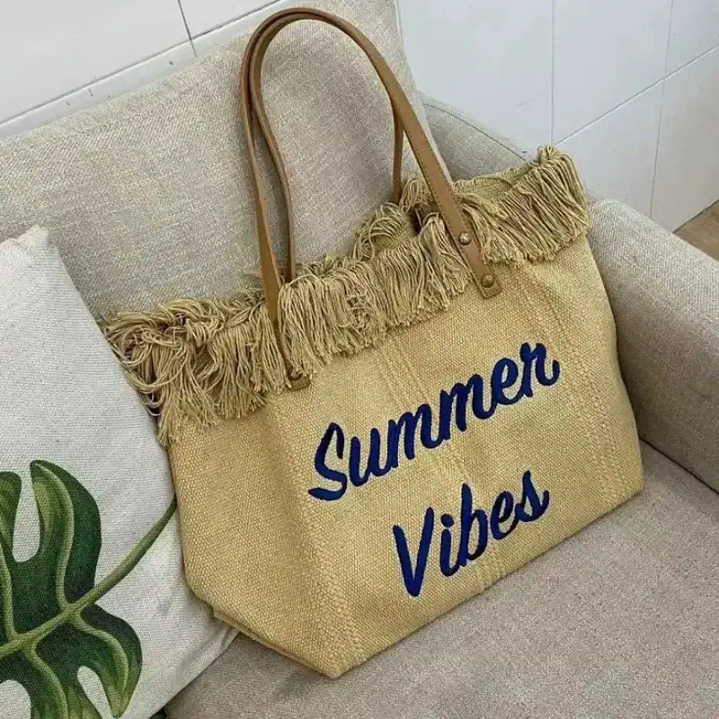 Rosa strandväska med text Summer Vibes, hängande på soffa med palmblad.