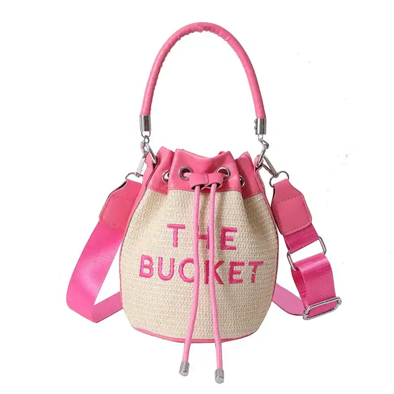 Rosa stråväska med dragkedja och skuldraslinga, texten THE BUCKET på framsidan.