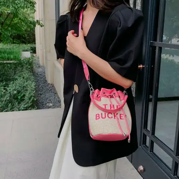 Rosa stråväska med dragkedja och text, bärt som axelväska.