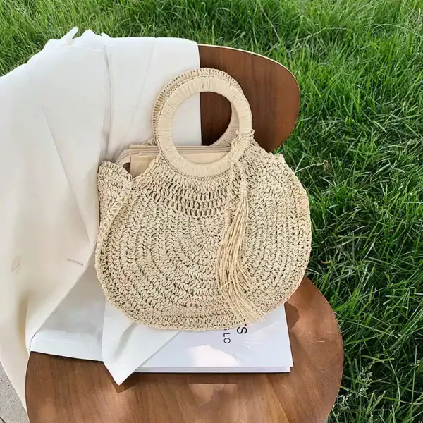 Rund halmväska med tofs, sommarväska, naturfärgad, sittande på trästol i gräs.