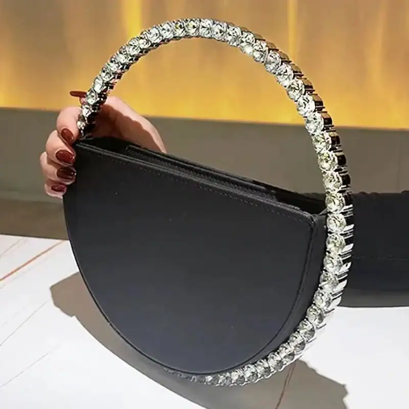 Svart rund clutch med strass på handtaget och kant, elegant axelväska.
