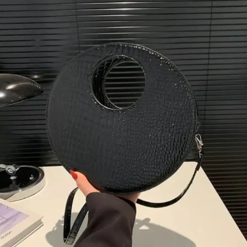 Svart rund väska med hål, axelväska med textur och axelrem.