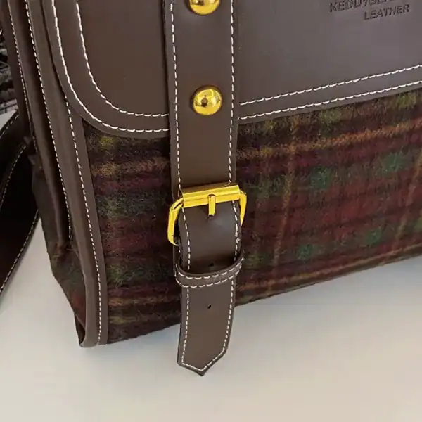 Rutig ryggsäck med brunt läder och guldpläterad snabbklick, detaljvy.
