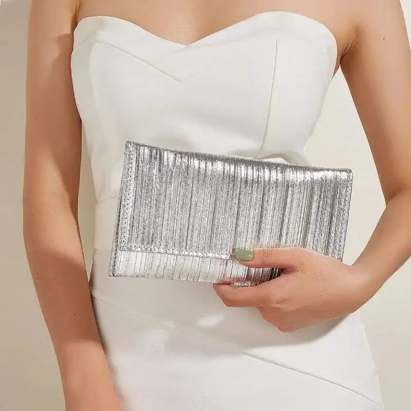 Silver plisserad clutch i handen, matchar vit klänning för fest.