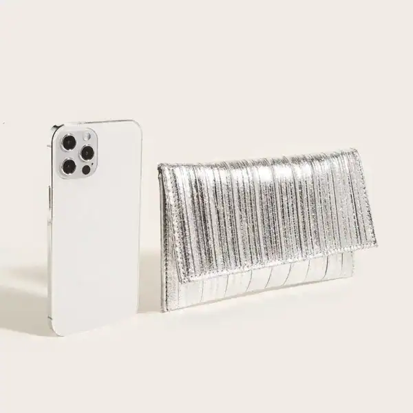 Silver plisserad clutch bredvid en vit mobiltelefon.