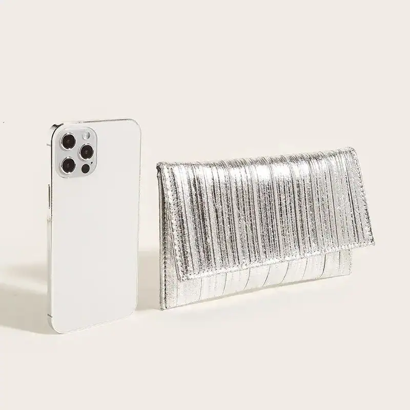 Silver plisserad clutch bredvid en vit mobiltelefon.