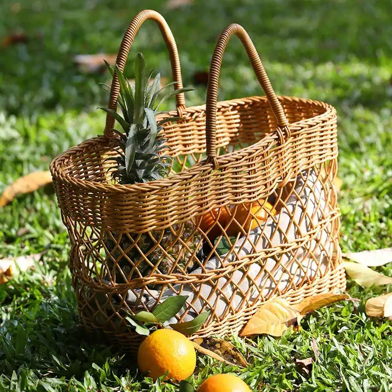 Stor korgväska i rattan med ananas och apelsiner på gräsmatta.
