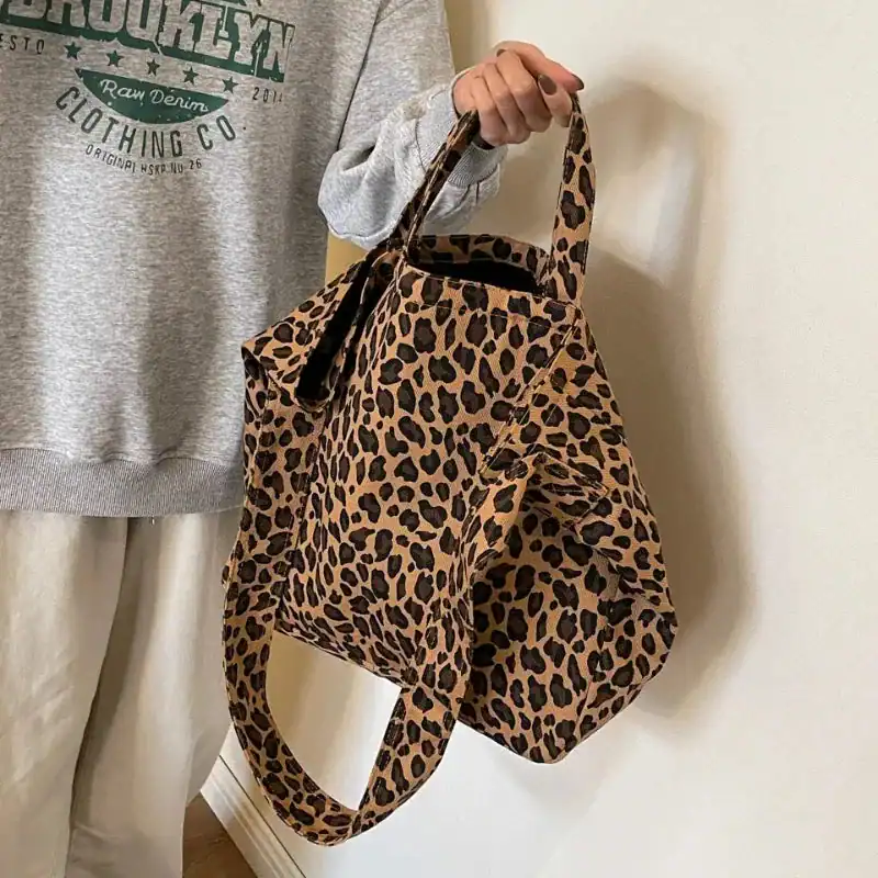 Stor leopard shoppingväska i beige och svart, hållen av en person i grå tröja.