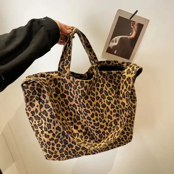 Stor leopard shoppingväska i beige och svart, hållen i handen mot vit vägg.