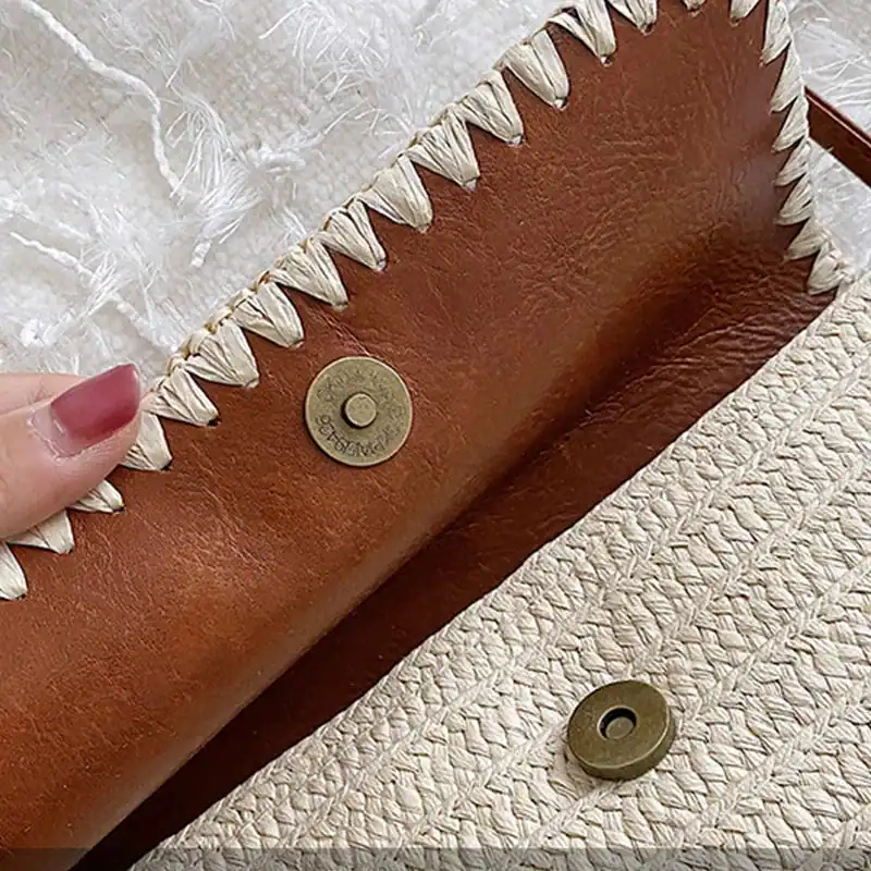 Stråväska med läderlock och metallknapp, detalj på handtag och sömmar.