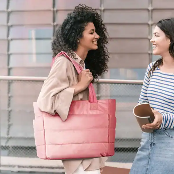 Svart datorväska med rosa färg, bärs av kvinna i stadslandskap.