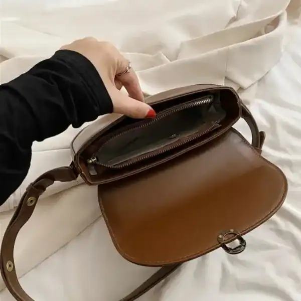 Svart halvmåneformad väska med lock och axelrem, kompakt modell.