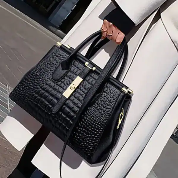 Svart handväska med krokodilmönster och guldtonad snäcka.