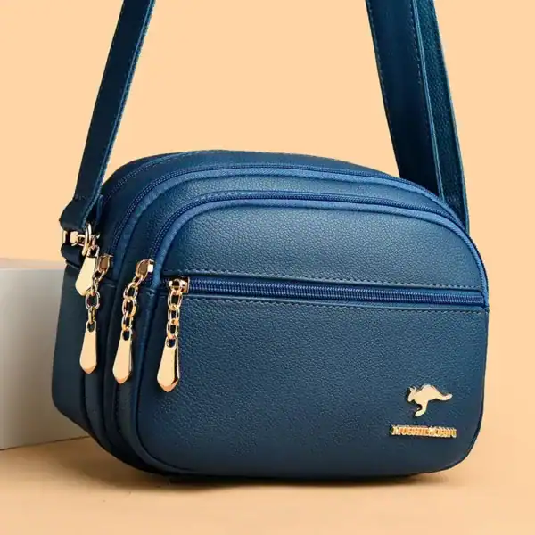 Svart liten crossbody väska med guld dragkedjor och metalldetalj.