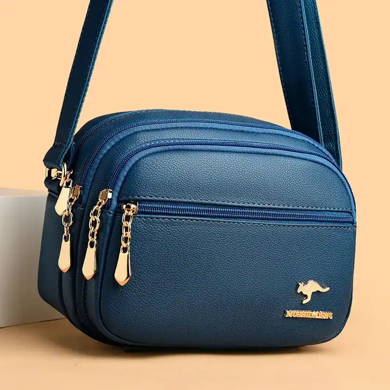 Svart liten crossbody väska med guld dragkedjor och metalldetalj.