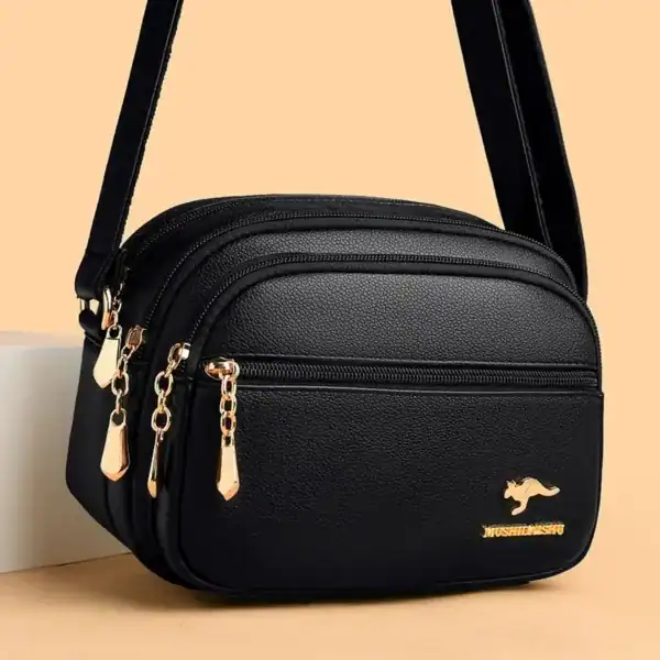 Svart liten crossbody väska med guld dragkedjor och metalldetalj.