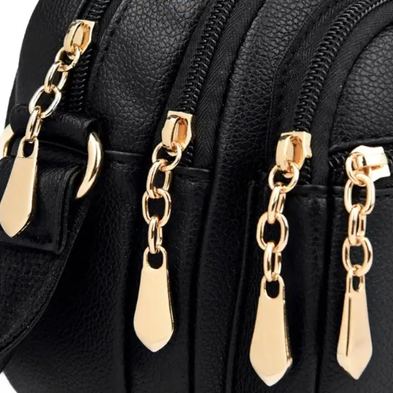 Svart liten crossbody väska med guld dragkedja och texturerat läder.