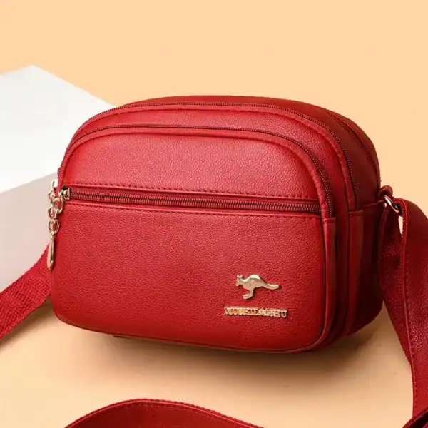Röd liten crossbody väska med axelrem och guldpläterad metalldetalj.
