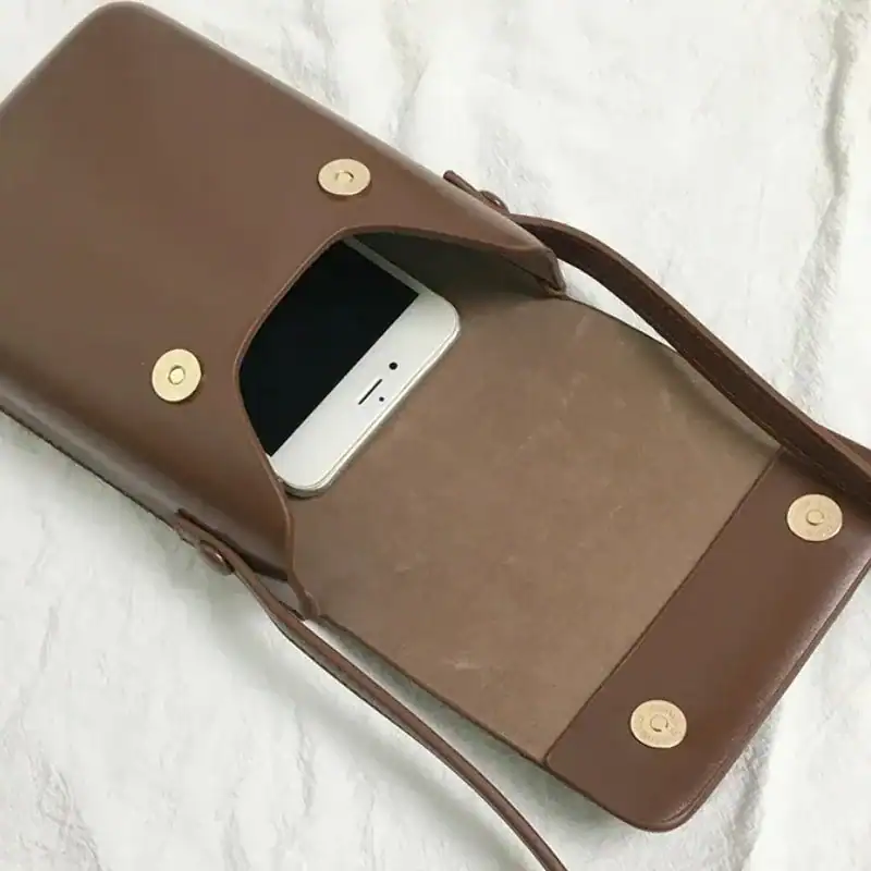 Svart mobilväska med telefon i fickan och guldplåt.
