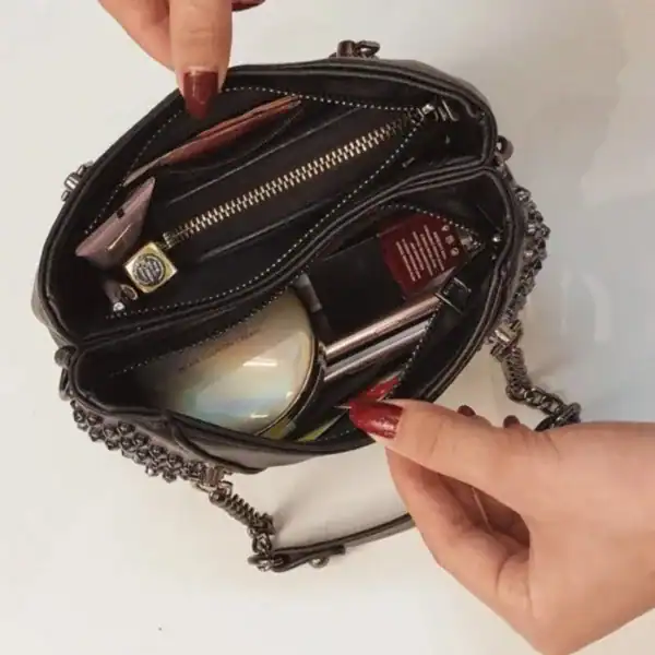 Svart nitväska med kedja, öppen och fylld med kosmetik och accessoarer.