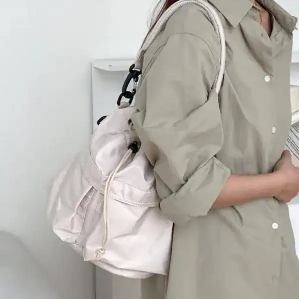 Svart nylon hinkväska, minimalistisk axelväska med dragkedja och vit axelrem.