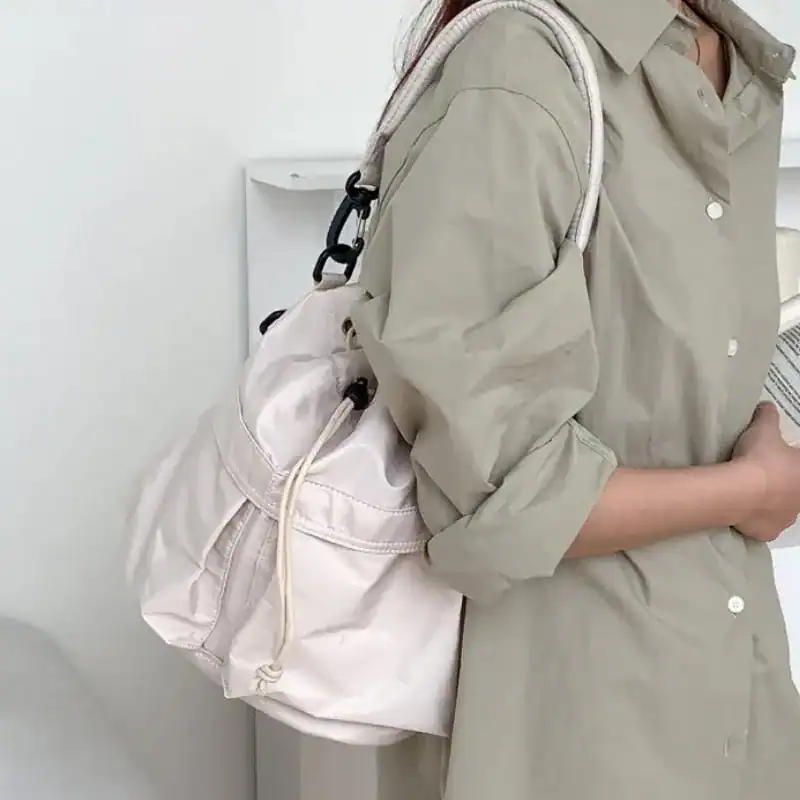 Svart nylon hinkväska, minimalistisk axelväska med dragkedja och vit axelrem.