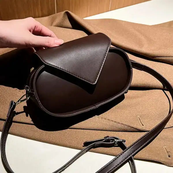 Svart oval axelremsväska med platt axelrem, läderliknande material och minimalistisk design.