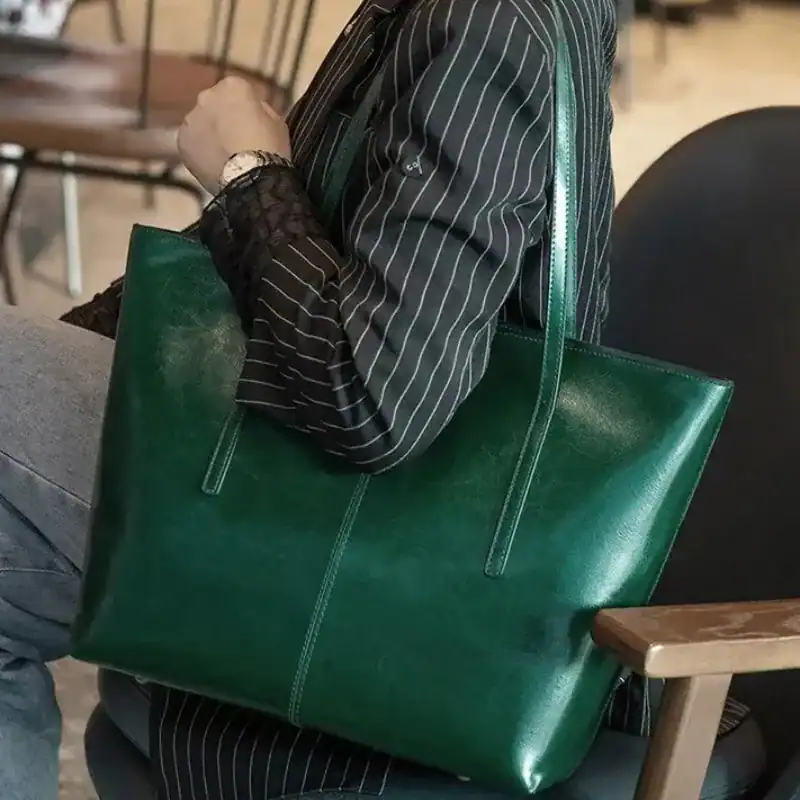 Svart tote shoppingväska i grön färg, hållen av en person i ståltrådsklädsel.