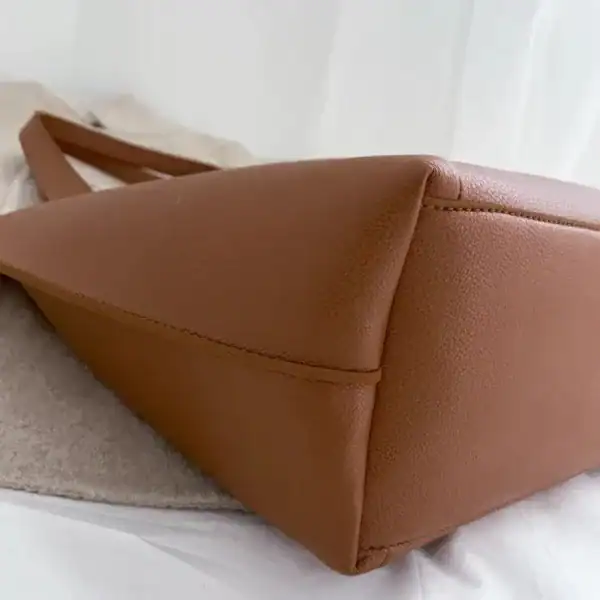 Svart tygshoppingväska i brunt läderliknande material med tydliga sömmar och elegant form.